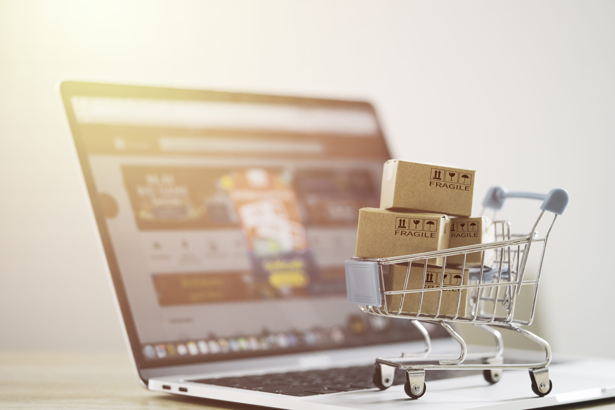 Mini shopping cart with cardboard boxes placed on a laptop representing e-commerce website development and online shopping | Webface